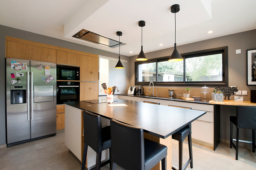 This is an example of a mid-sized contemporary l-shaped eat-in kitchen in Nantes with a drop-in sink, flat-panel cabinets, granite benchtops, beige splashback, ceramic floors, with island, beige floor, glass tile splashback, light wood cabinets and black appliances.