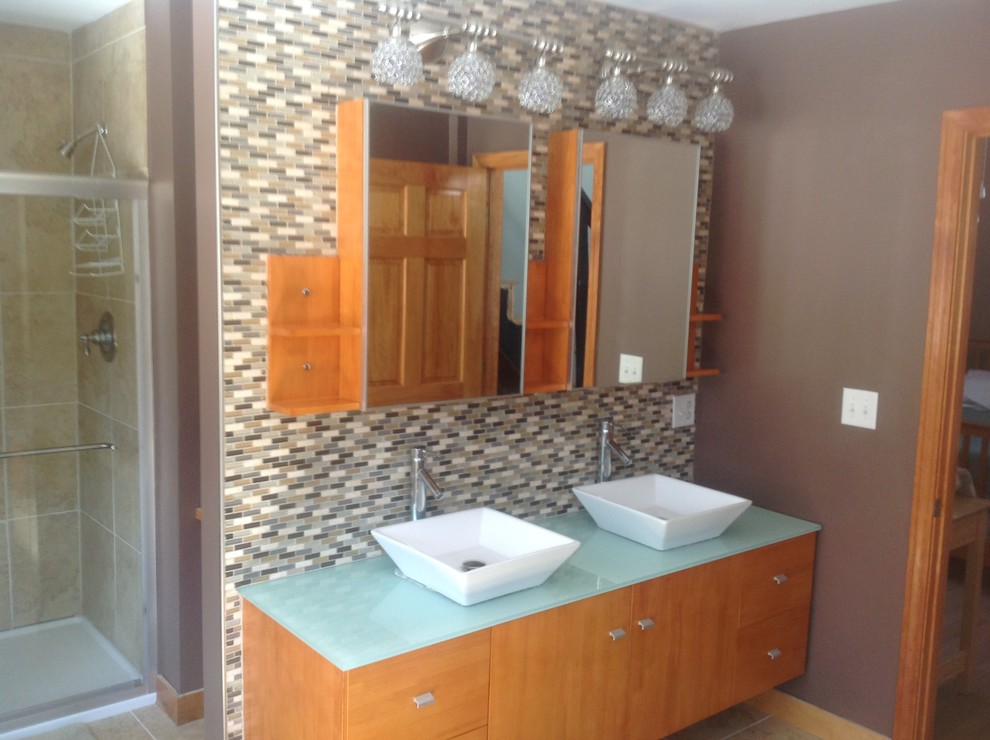 Photo of an expansive contemporary bathroom in Boston with a vessel sink, glass-front cabinets, medium wood cabinets, glass benchtops, a freestanding tub, a one-piece toilet, green tile, glass tile, brown walls, porcelain floors and with a sauna.