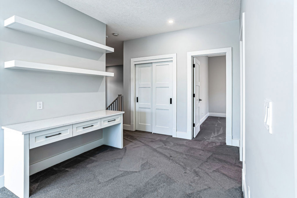 Home office - transitional built-in desk carpeted and gray floor home office idea in Calgary with white walls