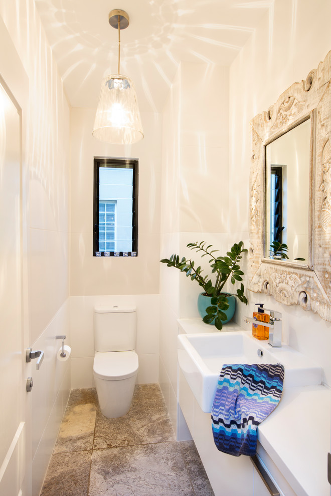 This is an example of a small eclectic powder room in Sydney with white cabinets, a one-piece toilet, white tile, ceramic tile, white walls, travertine floors, engineered quartz benchtops, grey floor and white benchtops.