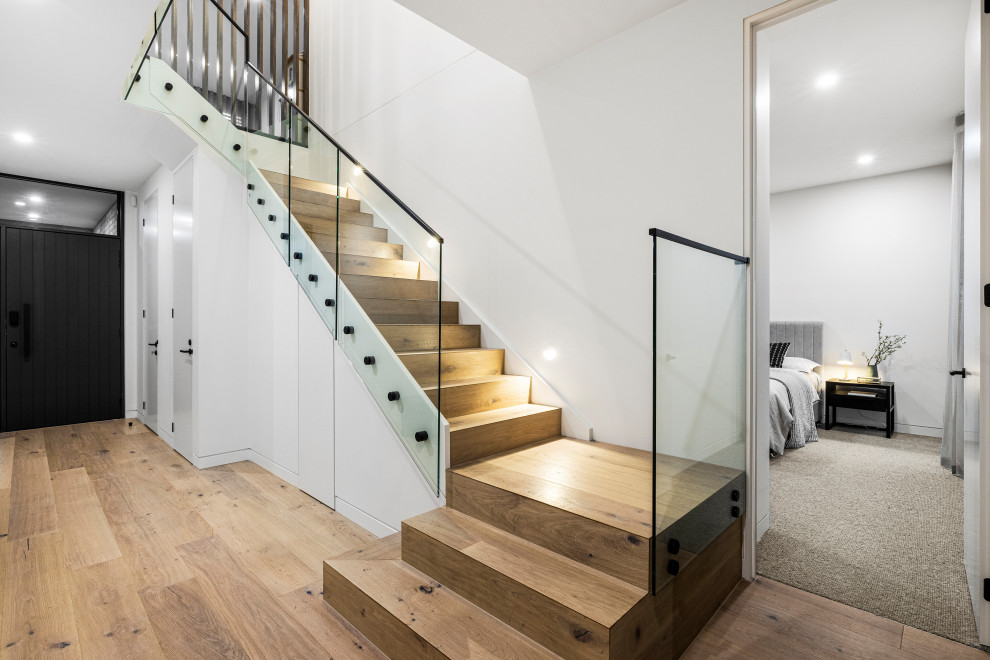 Imagen de escalera actual grande con escalones de madera, contrahuellas de madera y barandilla de vidrio