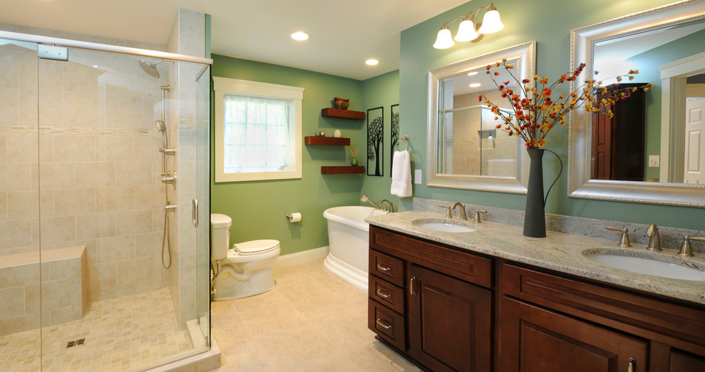Photo of a large transitional master bathroom in Cincinnati with raised-panel cabinets, dark wood cabinets, a freestanding tub, a corner shower, a two-piece toilet, stone tile, green walls, travertine floors, an undermount sink and limestone benchtops.