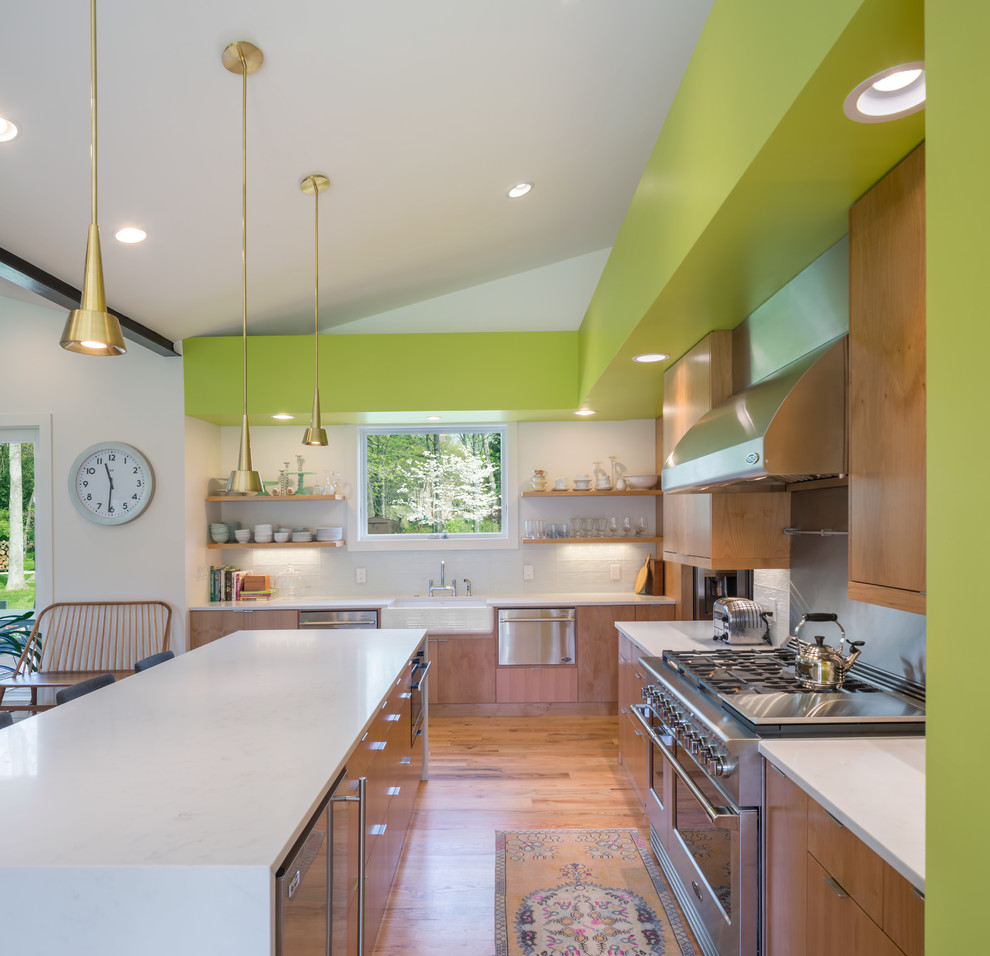 This is an example of a midcentury l-shaped kitchen in Charlotte with a farmhouse sink, flat-panel cabinets, medium wood cabinets, white splashback, stainless steel appliances, medium hardwood floors, with island and brown floor.