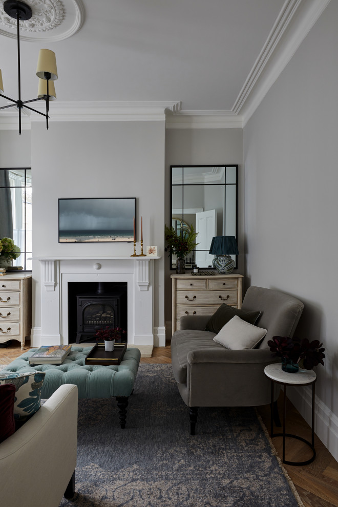 This is an example of a traditional formal living room in London with grey walls, medium hardwood floors, a wood stove, a wood fireplace surround and a wall-mounted tv.