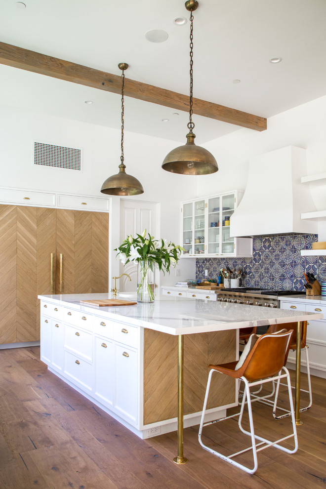 This is an example of a large transitional single-wall open plan kitchen in Los Angeles with a farmhouse sink, recessed-panel cabinets, white cabinets, marble benchtops, grey splashback, ceramic splashback, panelled appliances, light hardwood floors, with island and brown floor.