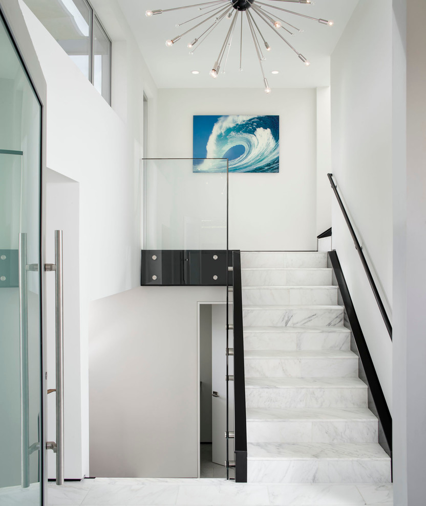 This is an example of a large beach style marble straight staircase in San Diego with marble risers and glass railing.