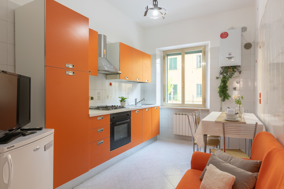 Photo of a small modern single-wall open plan kitchen in Other with a drop-in sink, flat-panel cabinets, orange cabinets, laminate benchtops, white splashback, porcelain splashback, black appliances, porcelain floors, no island, multi-coloured floor and white benchtop.