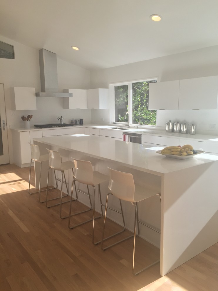 Mid-sized modern u-shaped open plan kitchen in Other with an undermount sink, flat-panel cabinets, white cabinets, solid surface benchtops, stainless steel appliances, light hardwood floors, with island and beige floor.
