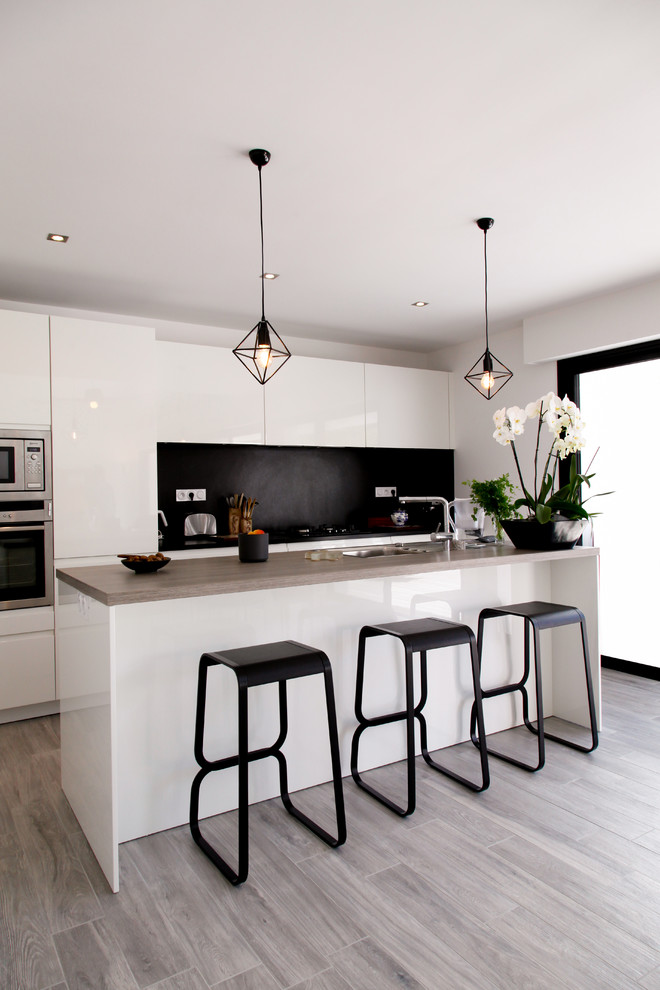 Design ideas for a mid-sized contemporary galley kitchen in Rennes with flat-panel cabinets, white cabinets, black splashback, stainless steel appliances, light hardwood floors and with island.