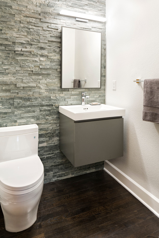Photo of a small transitional powder room in Denver with flat-panel cabinets, grey cabinets, a one-piece toilet, gray tile, stone tile, white walls, dark hardwood floors and a wall-mount sink.