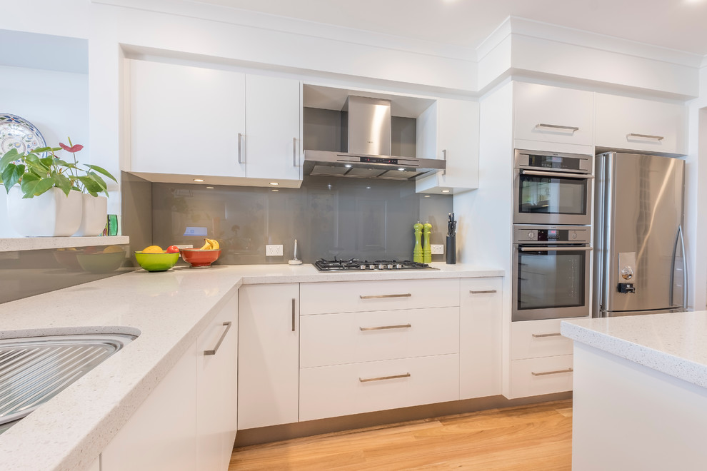 This is an example of a contemporary kitchen in Perth with an undermount sink, flat-panel cabinets, white cabinets, quartz benchtops, grey splashback, glass sheet splashback, stainless steel appliances, with island and white benchtop.