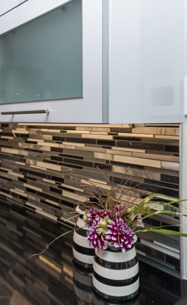 Large trendy u-shaped light wood floor open concept kitchen photo with an undermount sink, flat-panel cabinets, white cabinets, granite countertops, multicolored backsplash, mosaic tile backsplash, stainless steel appliances and an island