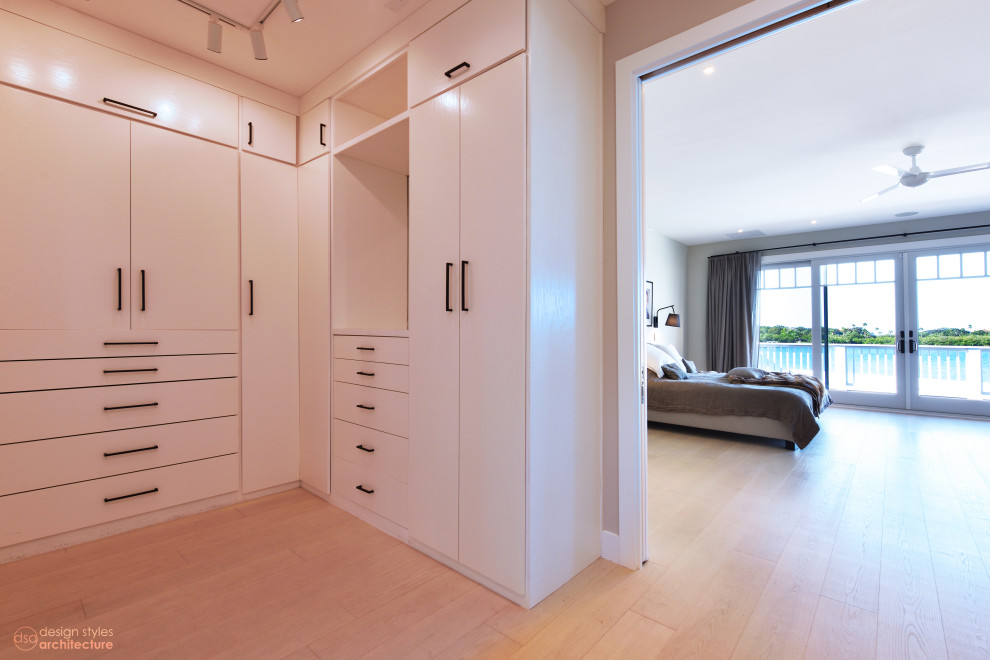 Photo of a contemporary gender-neutral dressing room with flat-panel cabinets, white cabinets and light hardwood floors.