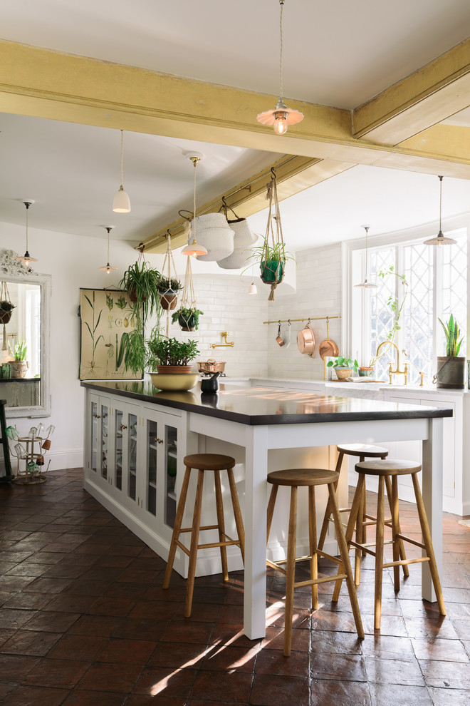 Design ideas for a large country kitchen in Other with a farmhouse sink, white cabinets, marble benchtops, white splashback, subway tile splashback, terra-cotta floors, with island, brown floor, glass-front cabinets and black benchtop.
