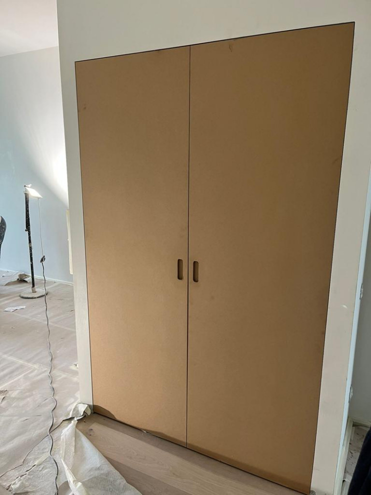 Cette image montre une petite buanderie linéaire minimaliste avec un placard, un placard à porte affleurante, des portes de placard blanches et des machines dissimulées.