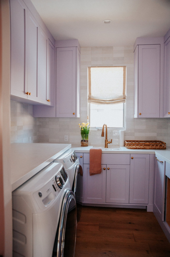 Example of a mid-sized classic u-shaped dark wood floor dedicated laundry room design in Los Angeles with a drop-in sink, shaker cabinets, quartz countertops, beige backsplash, ceramic backsplash, purple walls, a side-by-side washer/dryer and white countertops