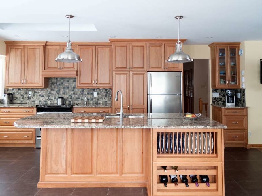 Mid-sized transitional single-wall porcelain tile and brown floor enclosed kitchen photo with a double-bowl sink, raised-panel cabinets, light wood cabinets, granite countertops, gray backsplash, glass tile backsplash, stainless steel appliances and an island