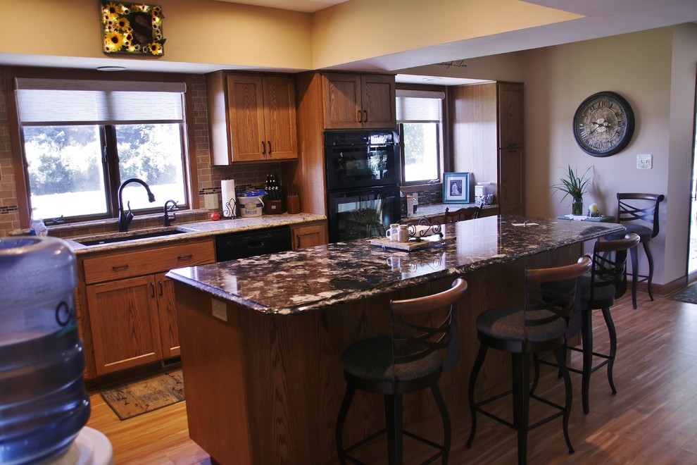 Mid-sized l-shaped eat-in kitchen photo with flat-panel cabinets, medium tone wood cabinets, quartz countertops, beige backsplash, black appliances and an island
