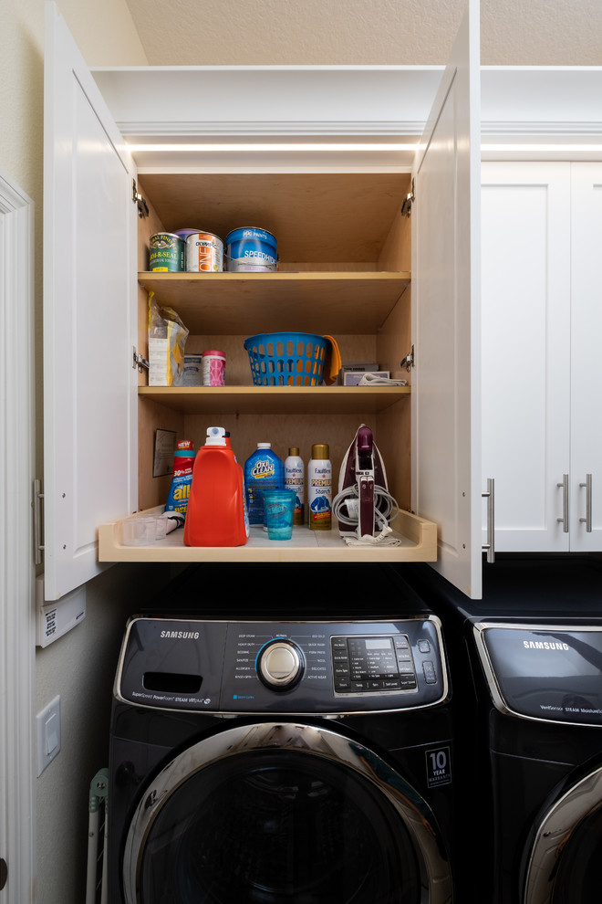 This is an example of a small transitional single-wall laundry cupboard in Tampa with shaker cabinets, white cabinets, beige walls, limestone floors, a side-by-side washer and dryer and beige floor.