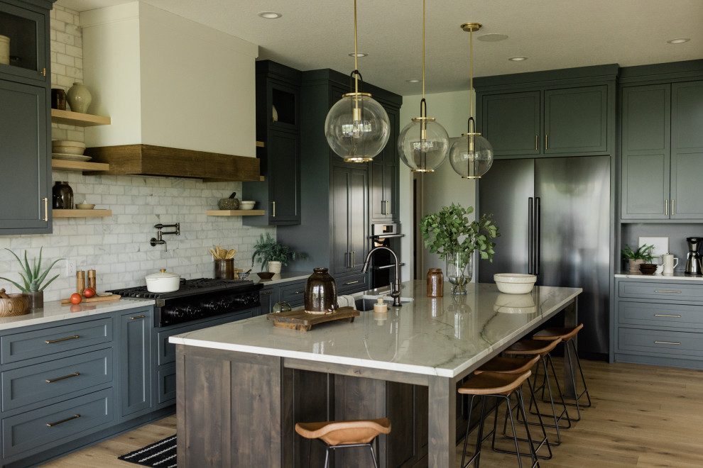 Large transitional l-shaped light wood floor open concept kitchen photo with an undermount sink, recessed-panel cabinets, gray cabinets, quartzite countertops, white backsplash, marble backsplash, black appliances, an island and white countertops