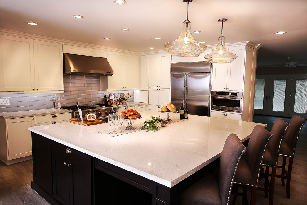 Inspiration for a large transitional u-shaped light wood floor kitchen pantry remodel with a farmhouse sink, shaker cabinets, white cabinets, quartz countertops, gray backsplash, glass tile backsplash, stainless steel appliances and an island