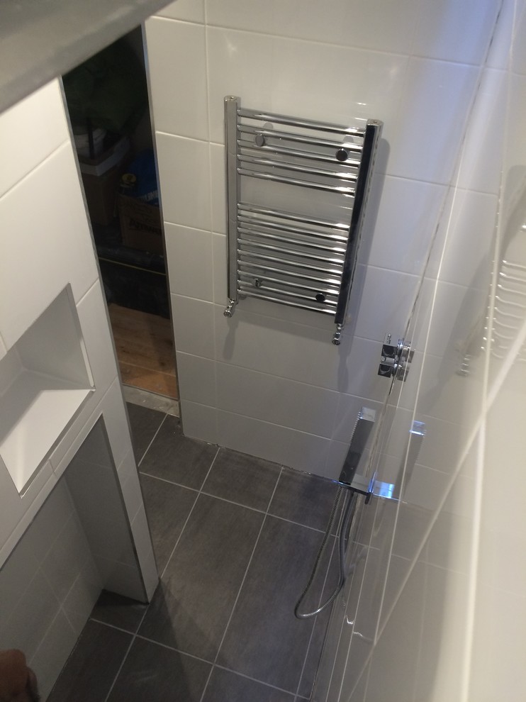 This is an example of a small contemporary 3/4 bathroom in London with a wall-mount sink, open cabinets, white cabinets, an open shower, a wall-mount toilet, white tile, ceramic tile, white walls and mosaic tile floors.