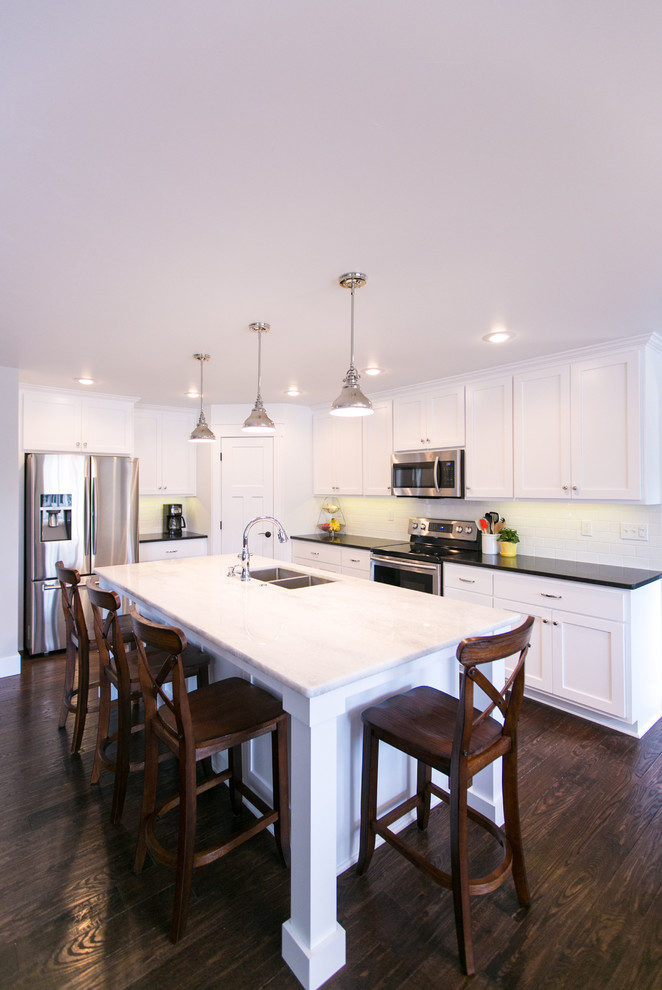 This is an example of an arts and crafts kitchen in Other with a double-bowl sink, flat-panel cabinets, white cabinets, quartzite benchtops, white splashback, subway tile splashback, stainless steel appliances, dark hardwood floors and with island.