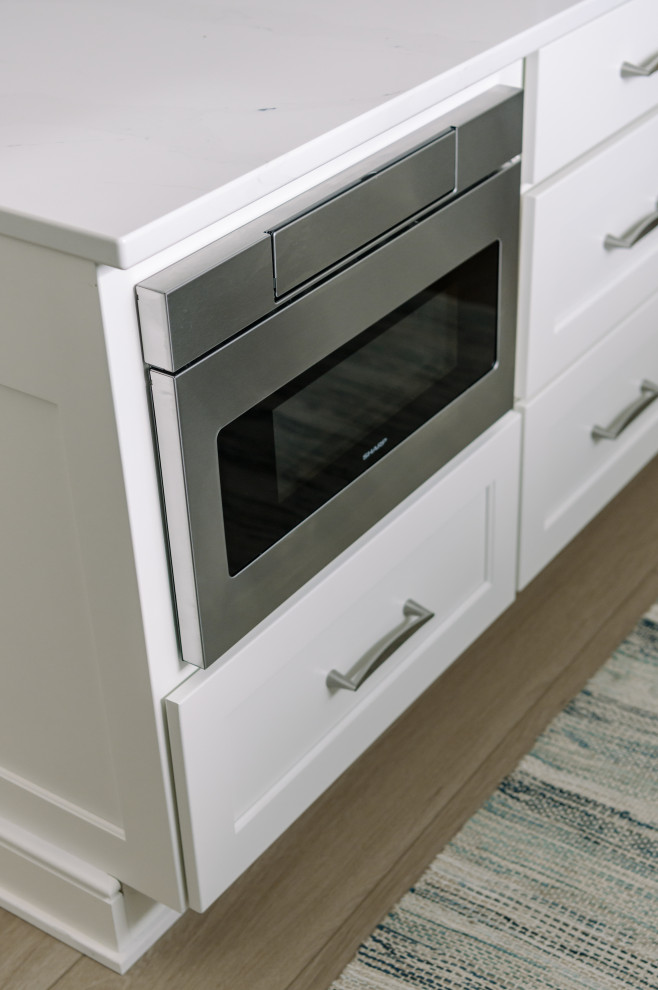 Inspiration for a large transitional l-shaped laminate floor and brown floor eat-in kitchen remodel with an undermount sink, shaker cabinets, white cabinets, quartz countertops, white backsplash, quartz backsplash, stainless steel appliances, an island and white countertops