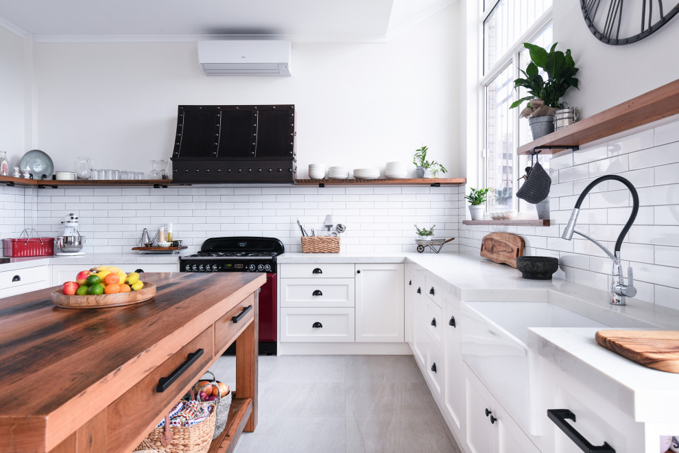 Large country u-shaped open plan kitchen in Sydney with a farmhouse sink, shaker cabinets, white cabinets, quartz benchtops, white splashback, ceramic splashback, coloured appliances, cement tiles, with island, grey floor and grey benchtop.