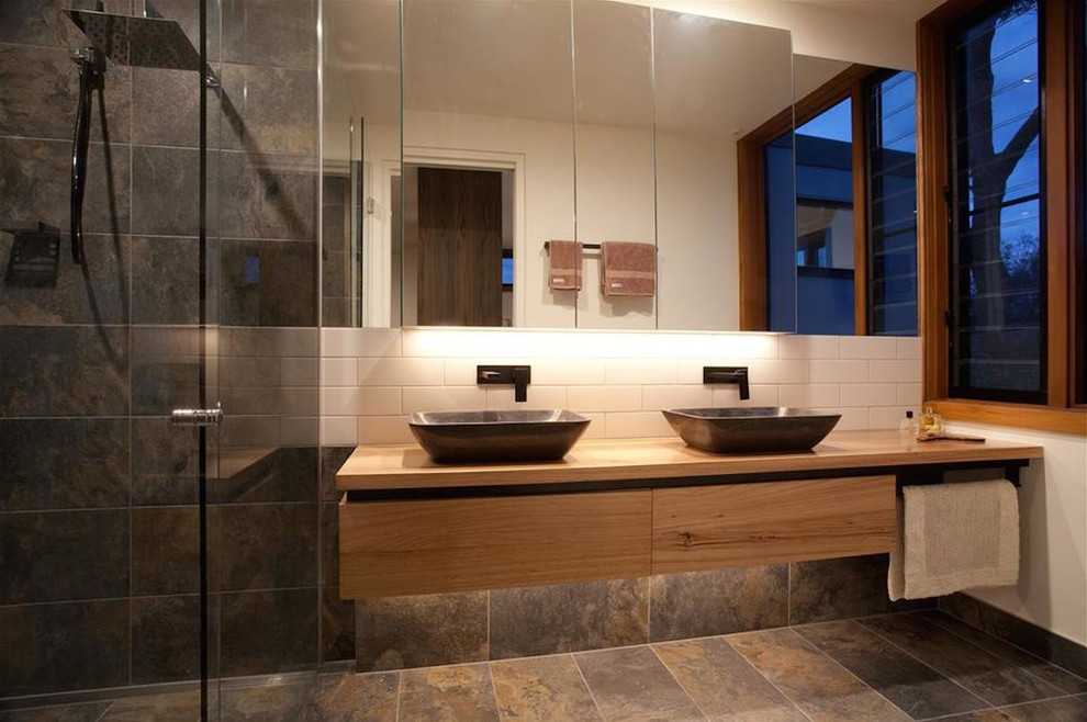 Photo of a large contemporary master bathroom in Melbourne with flat-panel cabinets, light wood cabinets, a corner shower, white tile, subway tile, white walls, slate floors, a vessel sink, wood benchtops and a hinged shower door.