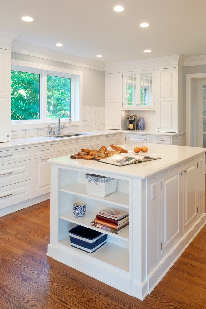 Photo of an expansive transitional u-shaped kitchen pantry in Richmond with a farmhouse sink, beaded inset cabinets, white cabinets, quartz benchtops, white splashback, subway tile splashback, stainless steel appliances, medium hardwood floors, multiple islands, brown floor and white benchtop.