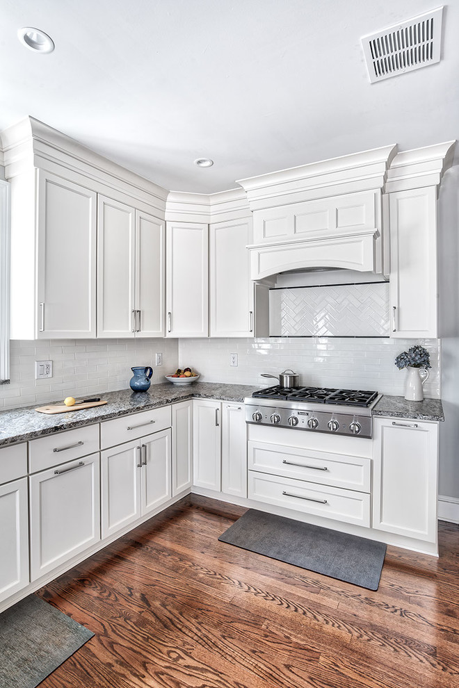 Photo of a large traditional u-shaped eat-in kitchen in New York with an undermount sink, beaded inset cabinets, white cabinets, granite benchtops, white splashback, subway tile splashback, stainless steel appliances, medium hardwood floors, a peninsula and grey benchtop.