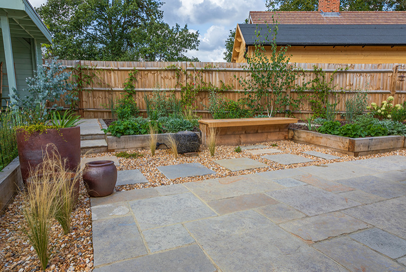 Diseño de jardín de estilo de casa de campo pequeño en verano en patio trasero con exposición total al sol, adoquines de piedra natural y con madera