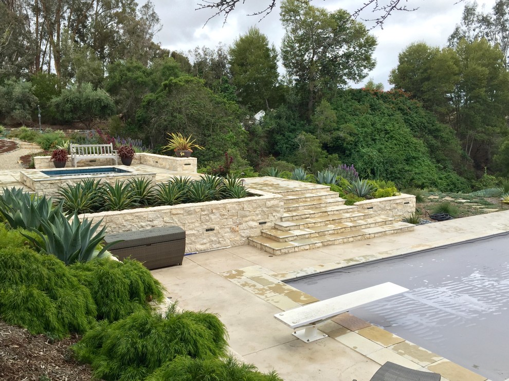 Expansive contemporary backyard full sun xeriscape in San Diego with a retaining wall and natural stone pavers.
