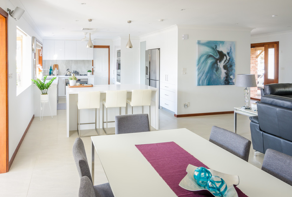 This is an example of a large modern l-shaped eat-in kitchen in Sydney with quartz benchtops, grey splashback, a double-bowl sink, flat-panel cabinets, white cabinets, ceramic splashback, stainless steel appliances, porcelain floors and with island.