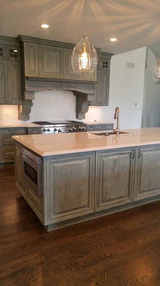 Large country eat-in kitchen in Chicago with an undermount sink, raised-panel cabinets, distressed cabinets, quartzite benchtops, panelled appliances, medium hardwood floors, multiple islands, brown floor and white benchtop.