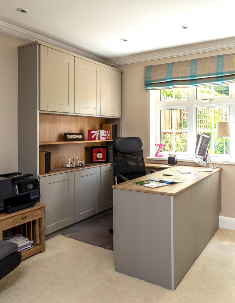 This is an example of a medium sized modern study in Hertfordshire with grey walls, carpet, a built-in desk and beige floors.