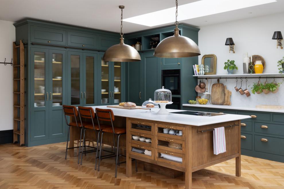 Inspiration for a large classic l-shaped kitchen/diner in London with a belfast sink, shaker cabinets, green cabinets, quartz worktops, white splashback, engineered quartz splashback, integrated appliances, medium hardwood flooring, an island and white worktops.