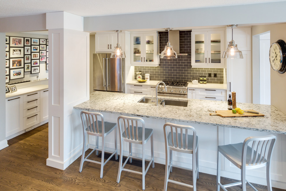 Example of a mid-sized transitional galley medium tone wood floor open concept kitchen design with an undermount sink, shaker cabinets, white cabinets, gray backsplash, stainless steel appliances, marble countertops, subway tile backsplash and a peninsula