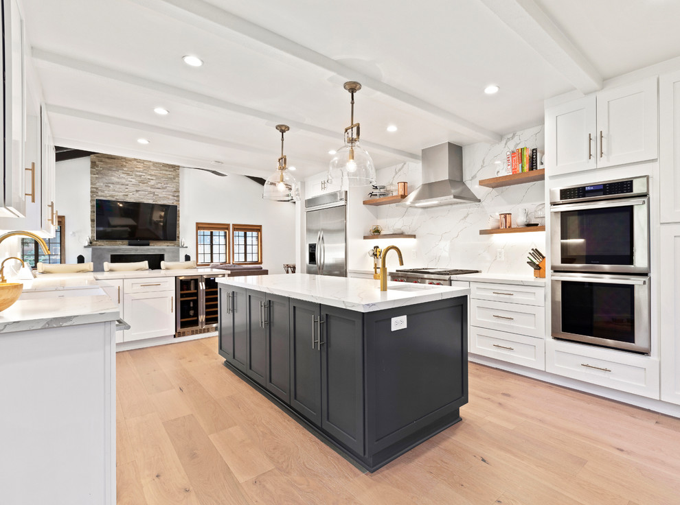 This is an example of a large transitional u-shaped open plan kitchen in Los Angeles with shaker cabinets, quartz benchtops, porcelain splashback, stainless steel appliances, light hardwood floors, with island, beige floor, white benchtop, an undermount sink, white cabinets and white splashback.