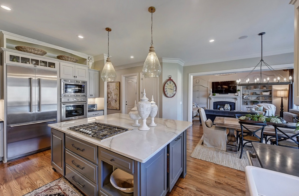 Large eat-in kitchen in Charlotte with a farmhouse sink, raised-panel cabinets, beige cabinets, quartzite benchtops, grey splashback, ceramic splashback, stainless steel appliances, medium hardwood floors, with island, brown floor and white benchtop.