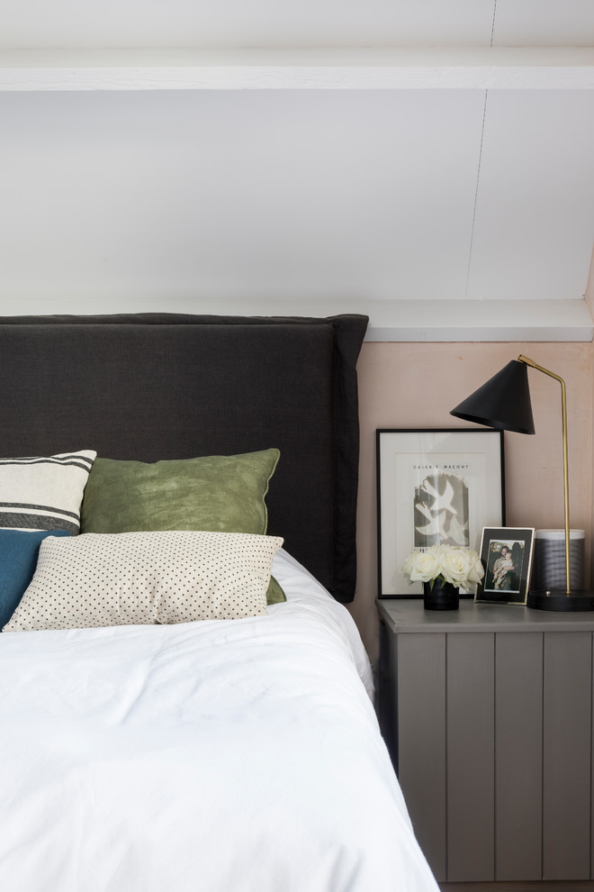 Photo of an industrial master and grey and pink bedroom in London with pink walls and light hardwood flooring.