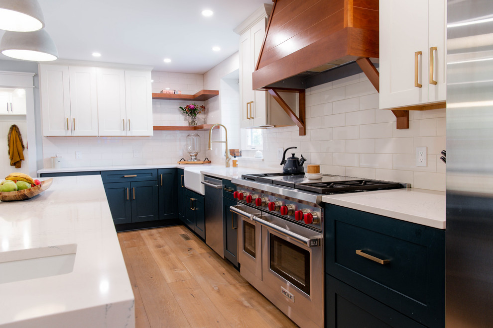 Expansive contemporary l-shaped kitchen pantry in New York with a farmhouse sink, shaker cabinets, green cabinets, quartz benchtops, white splashback, ceramic splashback, stainless steel appliances, light hardwood floors, with island and white benchtop.
