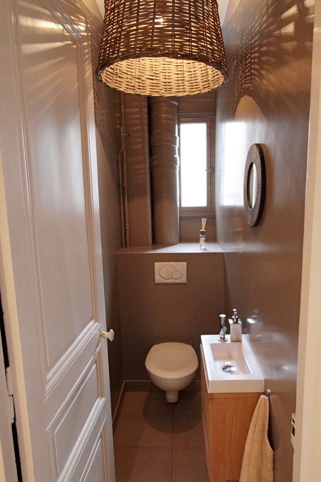 This is an example of a small transitional powder room in Paris with beaded inset cabinets, beige cabinets, a wall-mount toilet, grey walls, cement tiles, a trough sink and grey floor.