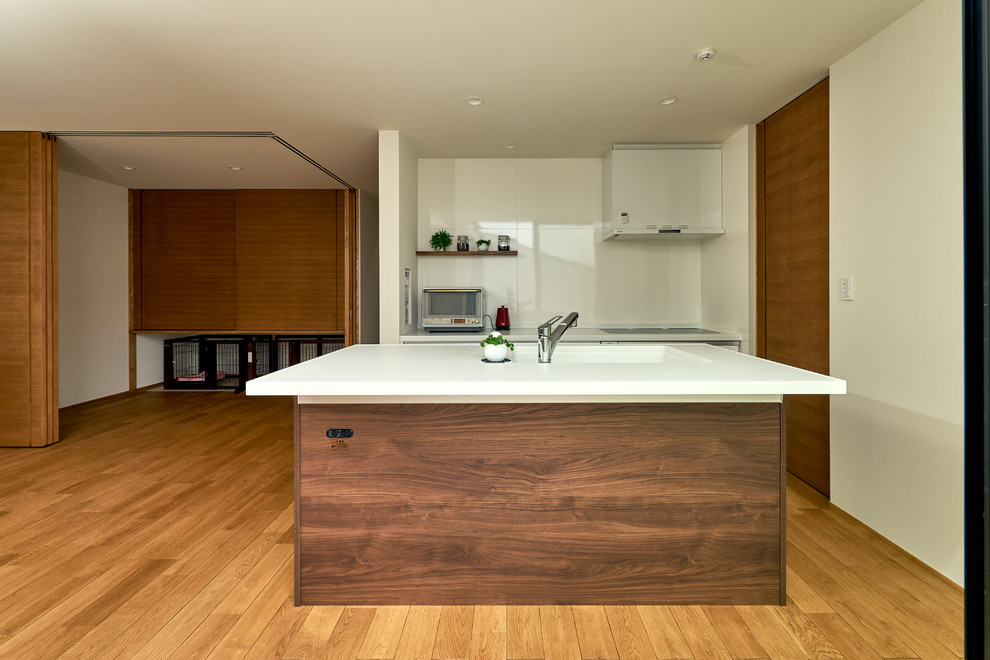 Foto de cocina moderna abierta con fregadero integrado, puertas de armario de madera en tonos medios, salpicadero blanco, electrodomésticos blancos, suelo de madera en tonos medios y una isla