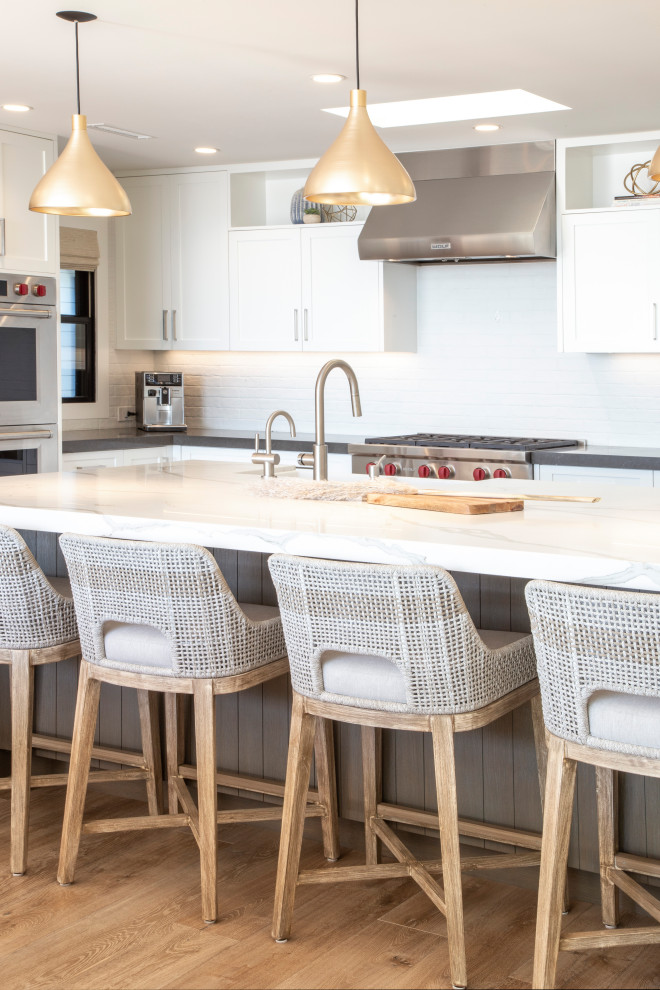 Open concept kitchen - transitional u-shaped open concept kitchen idea in Orange County with a farmhouse sink, shaker cabinets, white cabinets, quartz countertops, white backsplash, brick backsplash, stainless steel appliances, an island and white countertops