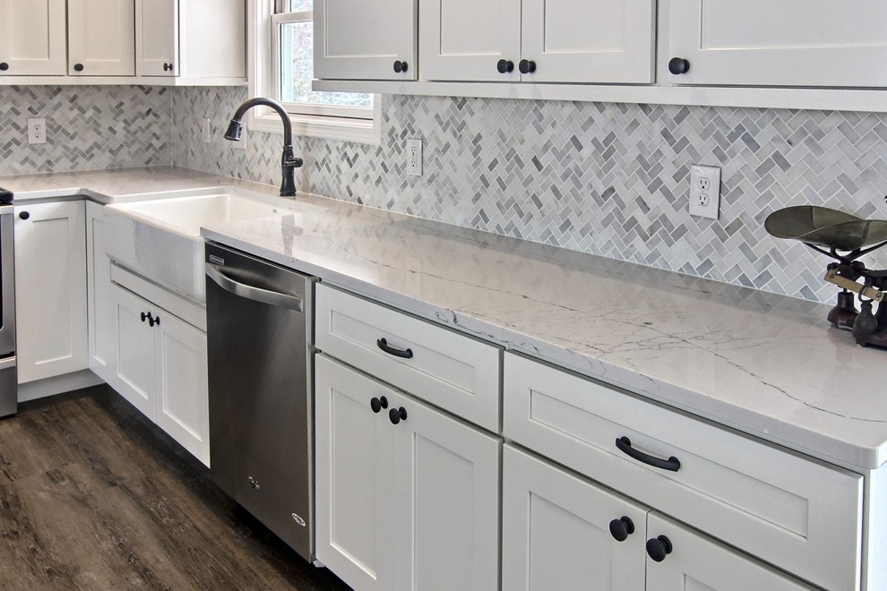 Inspiration for a mid-sized transitional l-shaped vinyl floor eat-in kitchen remodel with a farmhouse sink, shaker cabinets, white cabinets, quartz countertops, white backsplash, stone tile backsplash, stainless steel appliances and an island