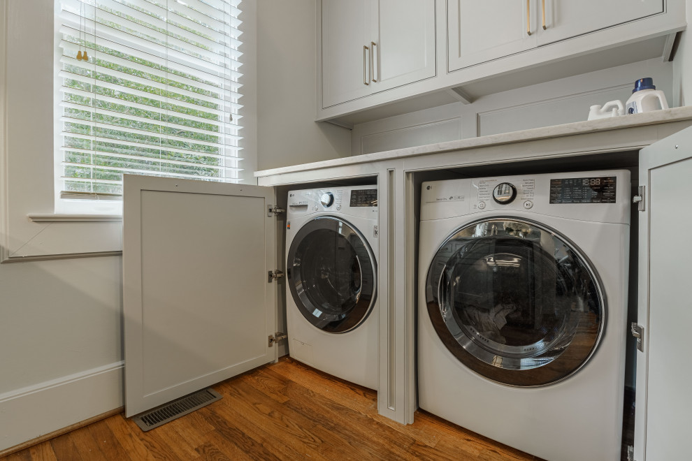 This is an example of a small transitional galley utility room in Other with beaded inset cabinets, grey cabinets, marble benchtops, metallic splashback, mirror splashback, white walls, dark hardwood floors, a side-by-side washer and dryer, brown floor and white benchtop.