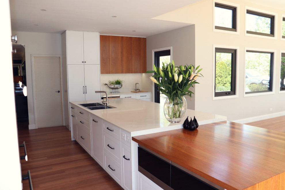 Design ideas for a mid-sized contemporary l-shaped eat-in kitchen in Canberra - Queanbeyan with a double-bowl sink, shaker cabinets, white cabinets, quartz benchtops, white splashback, stone slab splashback, black appliances, dark hardwood floors, with island, multi-coloured floor and white benchtop.