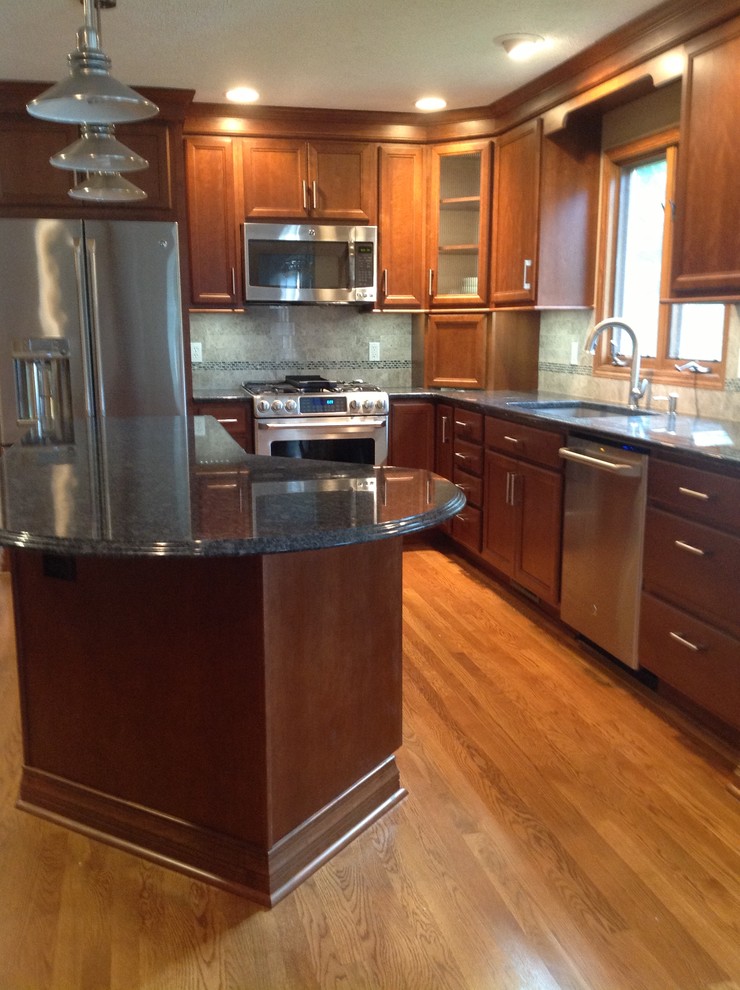 Example of a mid-sized transitional l-shaped medium tone wood floor eat-in kitchen design with an undermount sink, recessed-panel cabinets, medium tone wood cabinets, granite countertops, gray backsplash, stone tile backsplash, stainless steel appliances, gray walls and an island